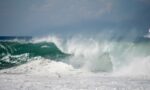 Japan Earthquake Tsunami Warning: दक्षिण जापान में 7.1 तीव्रता का भूकंप, 13 की मौत, मॉल ढहा Large ocean wave crashing on shore representing tsunami warning after Japan earthquake
